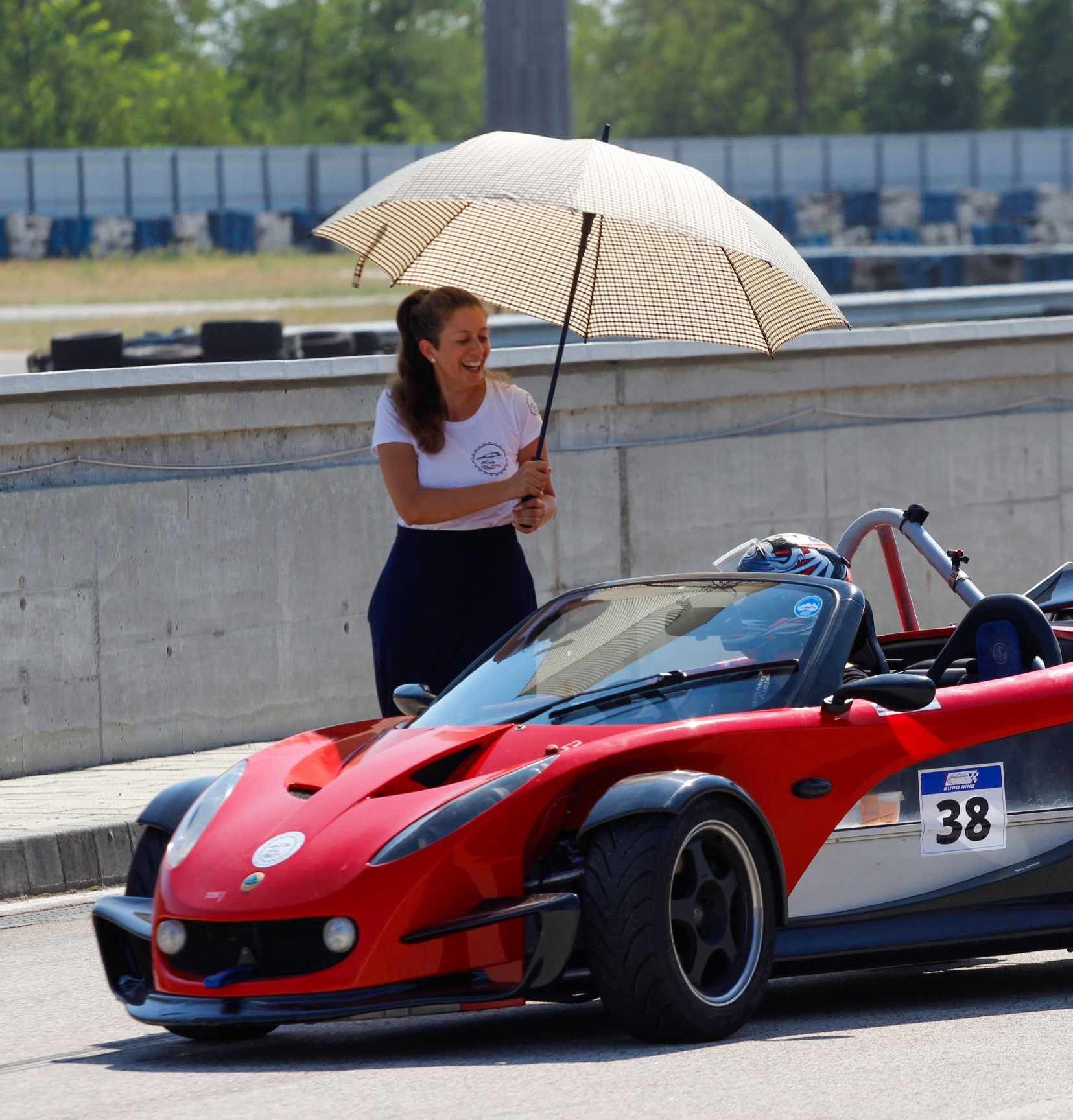 Red Lotus 340R by the pit wall, a woman beside it holding a parasol