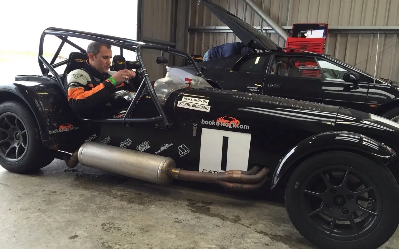 Driver strapped into a black race car in a pit garage