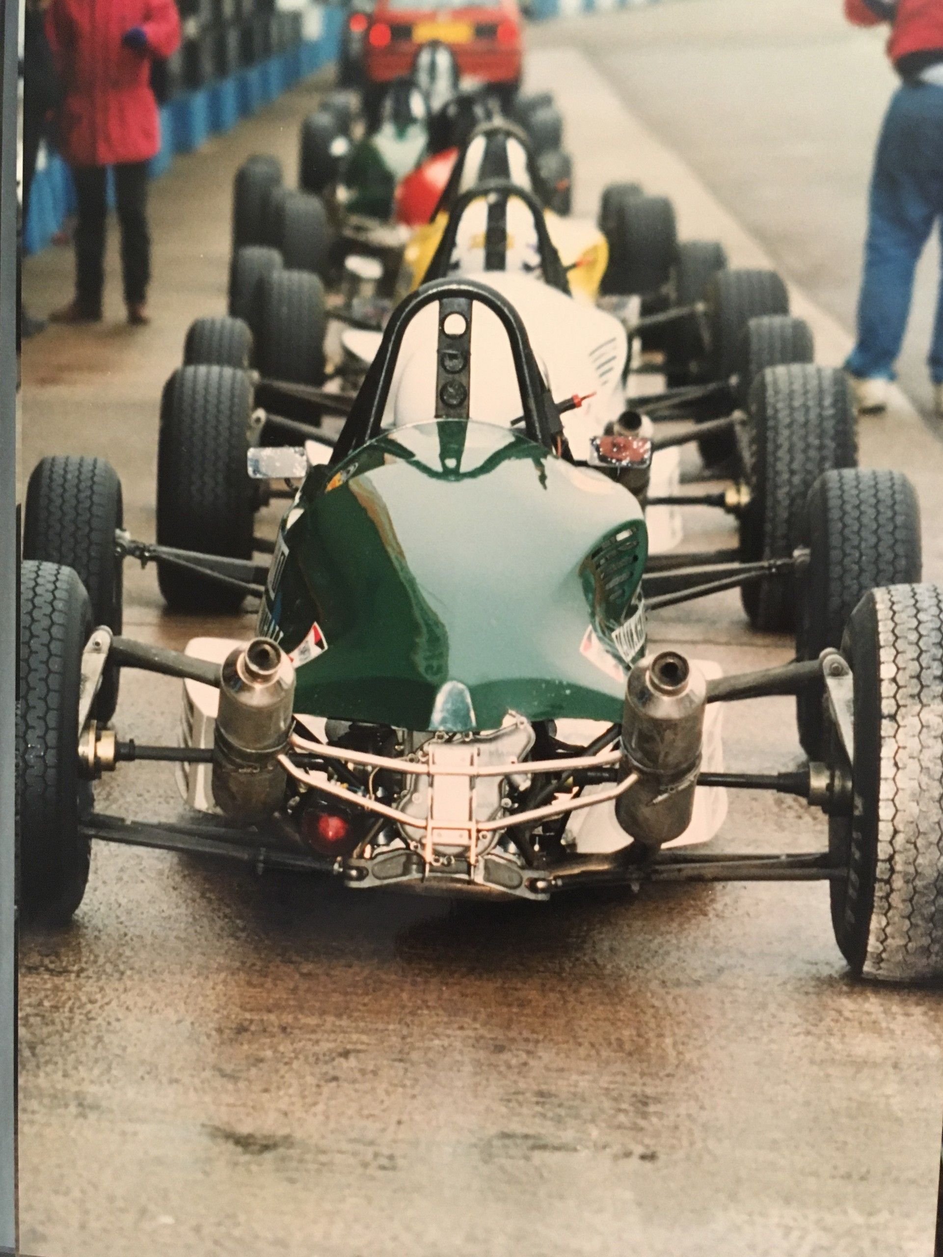 Green single-seater at the front of a queue in a wet paddock